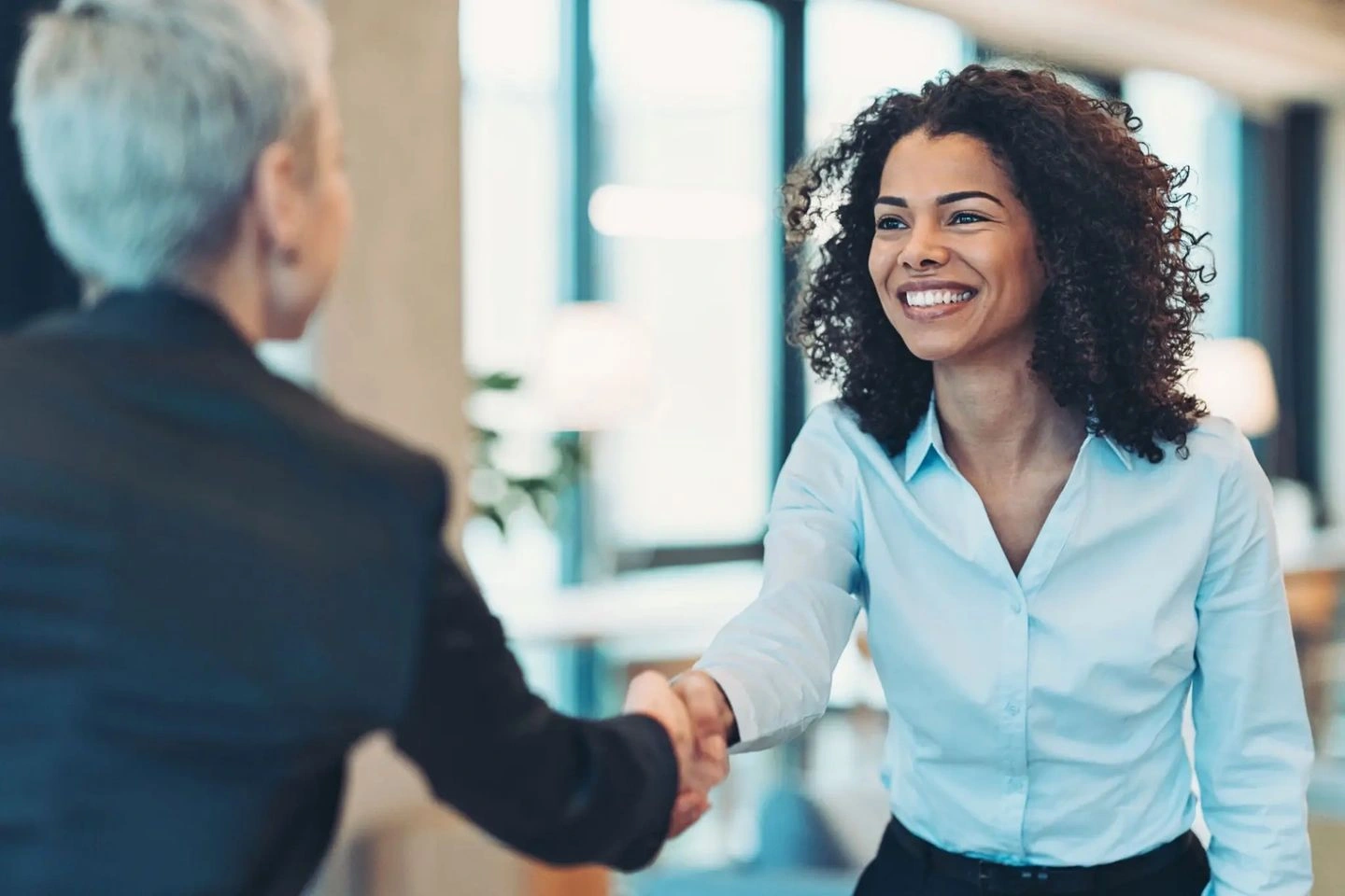 A woman and a man shaking hands with smiles in a professional setting.